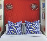 Bed with red headboard, blue patterned pillows, and decorative wall sconces. White bookshelves flank the bed.