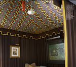 Room with patterned ceiling, brown walls and curtains, framed art, and decorative trim.