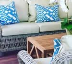 Wicker outdoor seating with cream cushions and blue patterned pillows, near a wooden coffee table.
