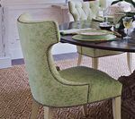 Green upholstered dining chair at a table, light wood legs, decorative trim.
