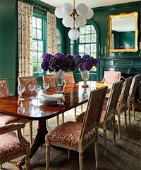 Elegant dining room with green walls, a long wooden table, and a chandelier.
