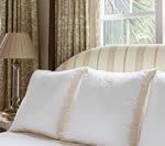 White pillows on a bed, next to a lamp and window with striped headboard and patterned curtains.