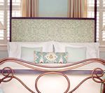 Bed with decorative headboard and pillows, near a window with shutters and curtains.
