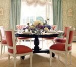 Round dining table with six chairs, floral arrangement, and pastel colored room.