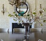 Elegant dining room with floral centerpiece, mirror, chandelier, and sconces.