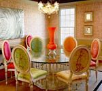 Dining room with a glass table and colorful chairs, vase.