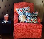 Bright red patterned armchair with blue pillows and stuffed bunny. Dark side table with tissue box and starfish.