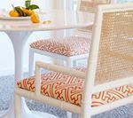 White dining chairs with patterned seat cushions around a white table, fruit on a plate.