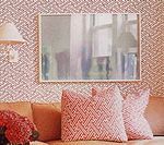 Pink patterned wallpaper with a rectangular mirror above a sofa with patterned pillows.