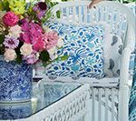 White wicker chair with patterned pillows and a vase of flowers.