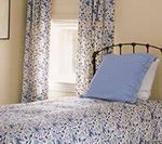 Bed with floral patterned bedding, curtains, and a blue pillow. Window in the background.