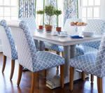 Dining table with blue patterned chairs, plants, and breakfast items in a well-lit room.