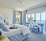 Bedroom with blue and white decor, bed, seating area, ocean view.