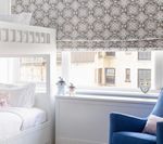 White bunk bed, blue armchair, window with patterned shade in a light-filled bedroom.