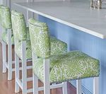 Four green patterned bar stools with white frames sit at a white countertop next to a blue wall.