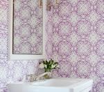 Bathroom with purple patterned wallpaper, white sink, and mirror. White flowers and jewelry on the counter.