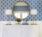 White cabinet with lamps, round mirror, floral wallpaper backdrop.