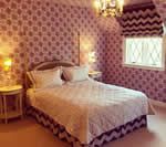 Bedroom with patterned mauve wallpaper, bed with white bedding, and small side tables.