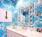 Bathroom with blue floral wallpaper, white vanity, mirror with a decorative frame, and framed artwork.