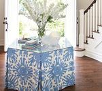Blue patterned skirted table with glass top, flowers, books, near a staircase.
