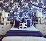 Bedroom with blue patterned wallpaper and bedding; white nightstands with lamps.