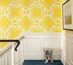 Yellow patterned wallpaper in a hallway with white wainscoting, a blue rug, and a decorative stool.