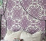 Bed with white pillows and patterned purple and white wallpaper backdrop.