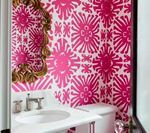 Pink floral patterned wallpaper in a small bathroom with a white sink, toilet, and gold mirror.