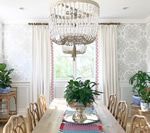 Dining room with long wooden table, chandelier, plants, and patterned wallpaper.