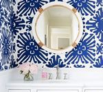 Round mirror with white frame and nautical rope detail over a white vanity, blue patterned wallpaper.