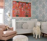 Nursery with a white crib, pink armchair, and llama toy, decorated with patterned wallpaper and colorful art.