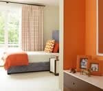 Bedroom with orange accents: bed, walls, frames, and bedding; beige and white curtains, natural light.