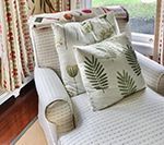 Armchair with patterned cushions; light colors and leaf designs, near a window with patterned curtains.