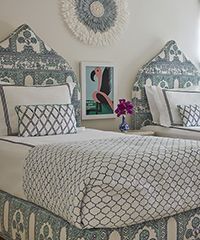 Twin beds with patterned teal and white bedding, flamingo art, and a woven wall hanging.