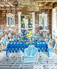 Blue and white outdoor dining table set under woven light fixtures.