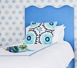 Blue headboard with scalloped edge, white bedding, patterned pillow, and matching wallpaper.