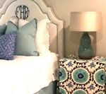 Bed with blue pillows, a patterned ottoman, and a teal lamp.