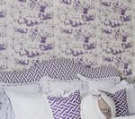 Bed with patterned purple and white wallpaper and pillows.