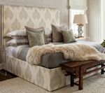 Beige upholstered bed with patterned headboard, layered bedding, and decorative pillows.