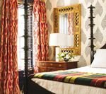 Bedroom with patterned wallpaper, gold mirror, red curtains, and bed with blanket.