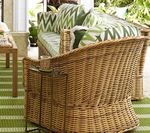 Wicker outdoor sofa with green patterned cushions, on a green striped rug, patio setting.