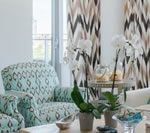 Living room with patterned curtains, armchairs, and orchids on a table.