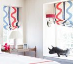 Bedroom with white walls, windows with patterned Roman shades, a bedside table, and a rhino figurine.