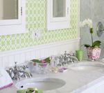 Bathroom with white double sink, chrome faucets, green patterned wallpaper, and orchid in a pink pot.
