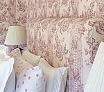 Bed with floral-patterned headboard and pillows in a room with matching wallpaper, and lamps.