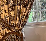 Brown and cream toile curtains draped next to a window; ornate chair in foreground.