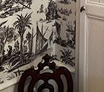 Dark brown chair in front of a wall with black and white scenic wallpaper, next to a white door frame.