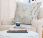 Cream armchair with decorative pillow, books, and tea cup on a white ottoman.