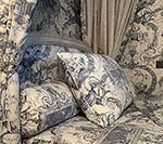 Blue and white toile cushions on a patterned sofa, curtains in the background.