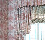 Pink patterned curtains and valance over a window with a green and white plaid shade.